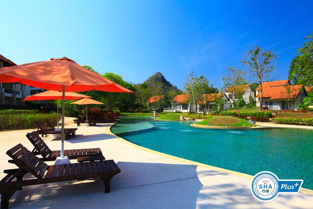 ein paar Bänke mit einem Regenschirm neben einem Pool in der Unterkunft Belle Villa Resort, Khao Yai in Mu Si