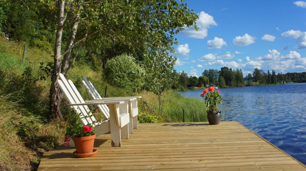 Sweden Slow Living في Gösunda: مرسى خشبي مع كرسيين وزهور على البحيرة