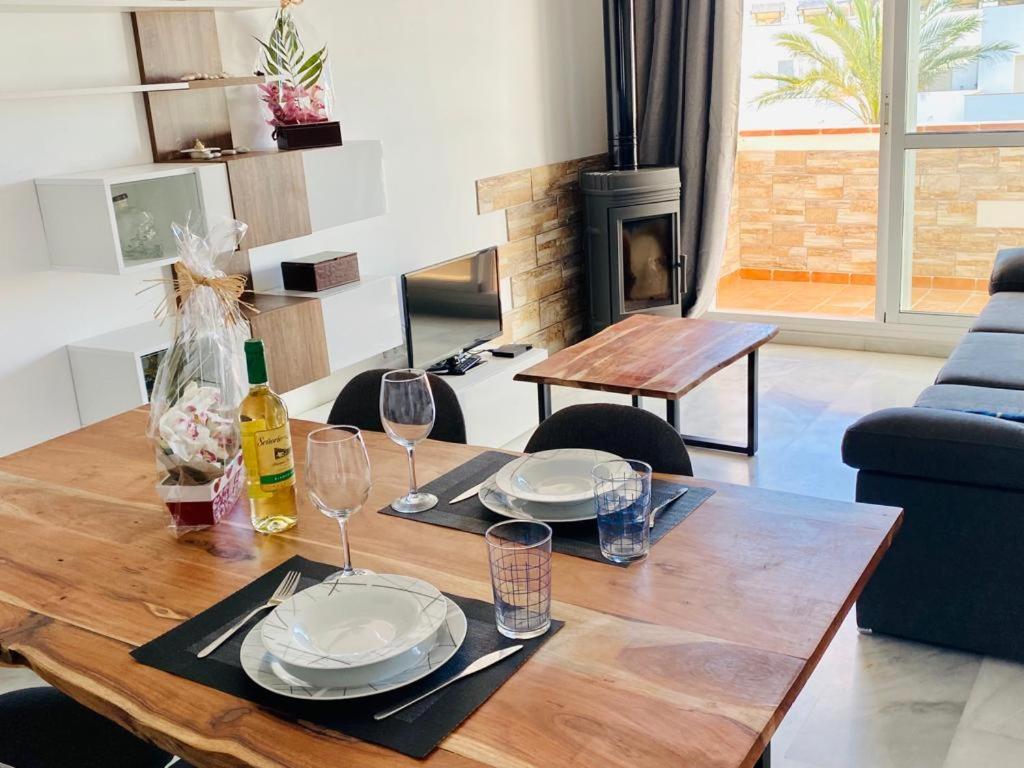 a wooden table with plates and wine glasses on it at Encantador ático con chimenea y piscina en Almería in Retamar