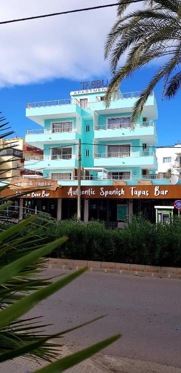 a large building with a palm tree in front of it at Tabbu ibiza apartments in Playa d'en Bossa