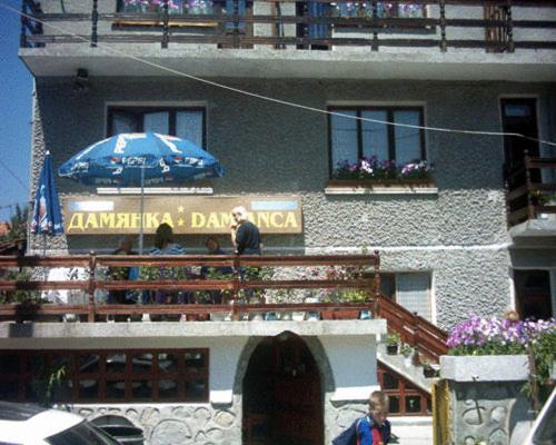 Dos personas sentadas en un balcón con sombrilla en Damianka Guest House, en Bansko