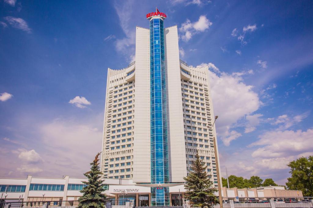 ein hohes weißes Gebäude mit einem roten Schild oben in der Unterkunft Belarus Hotel in Minsk