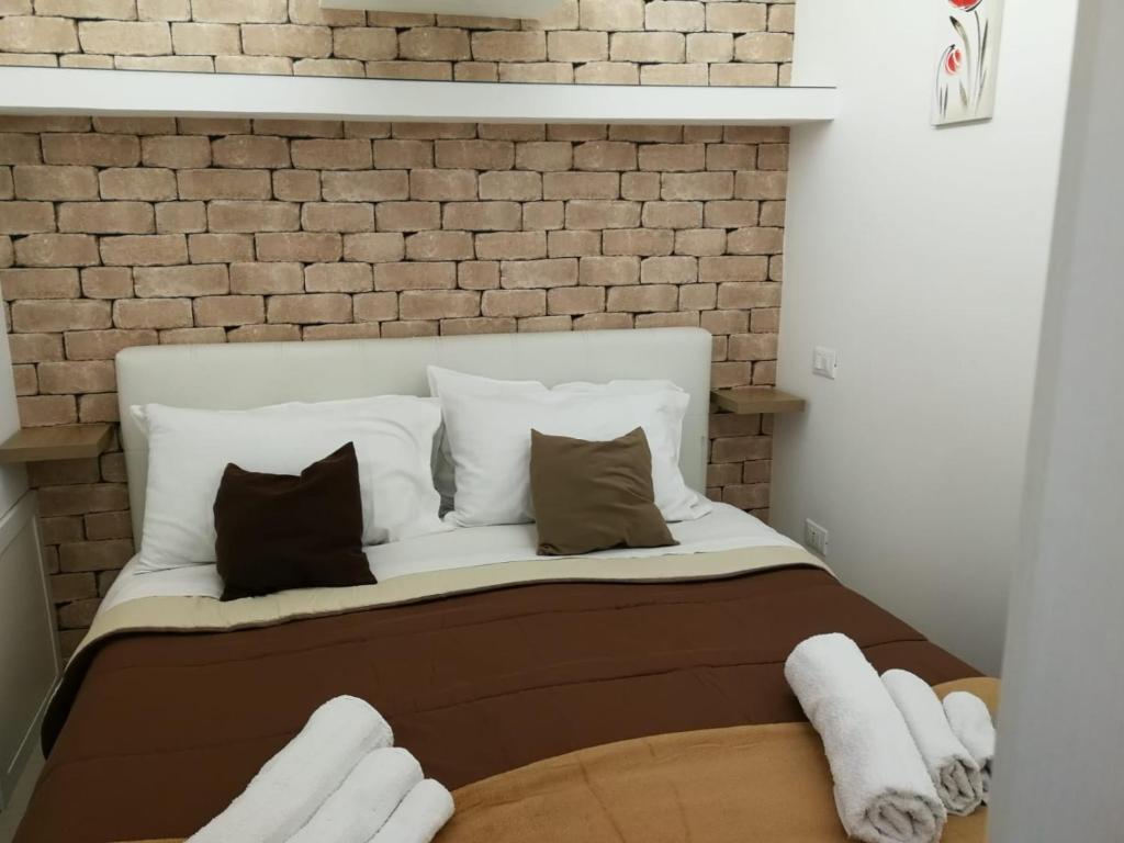 a white bed with pillows and a brick wall at BAARIA House Hotel in Barcellona-Pozzo di Gotto