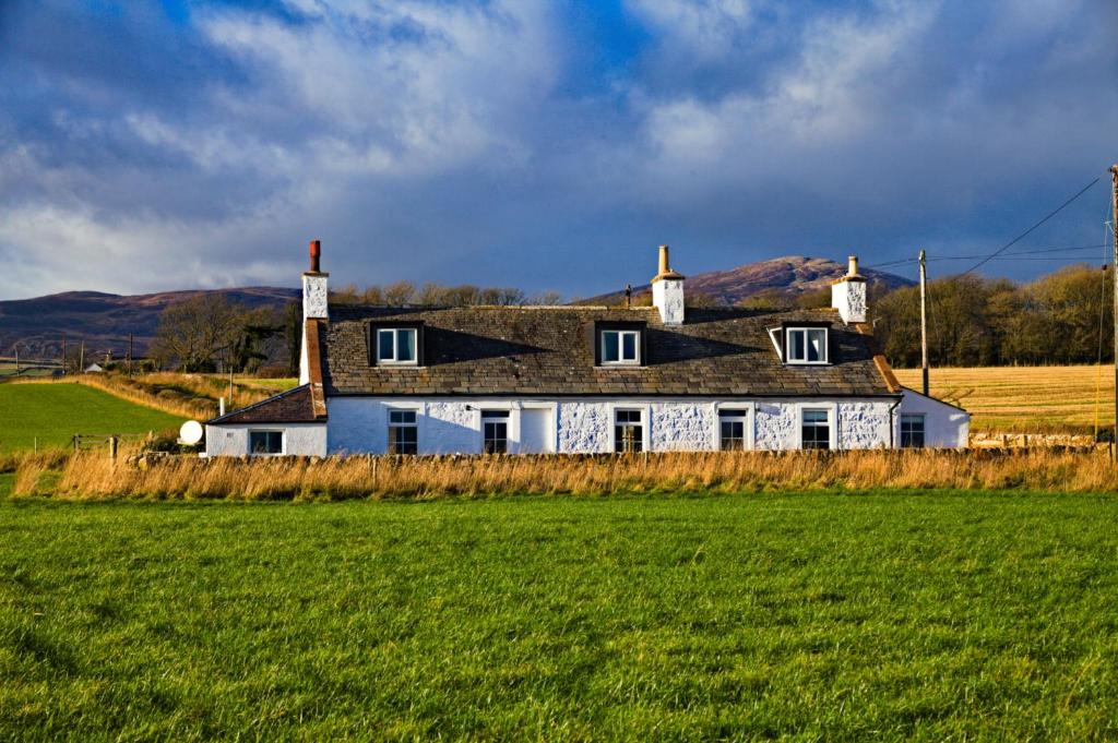 a house in the middle of a green field at Powillimount Cottage in Kirkbean