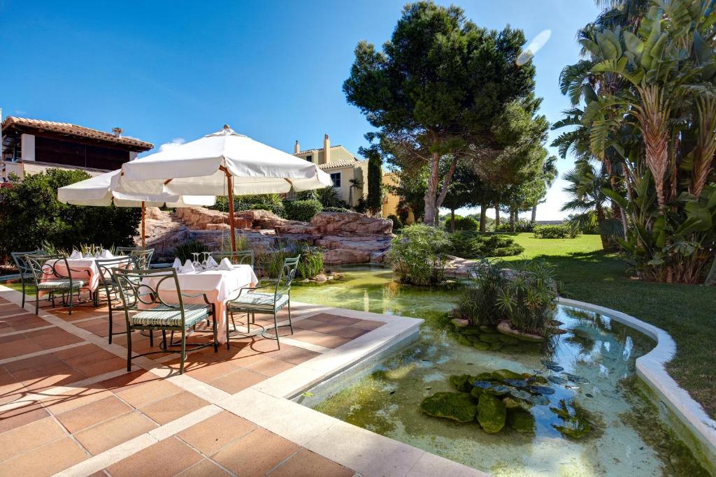 a patio with a table and an umbrella and a pond at Grupotel Playa Club in Son Xoriguer
