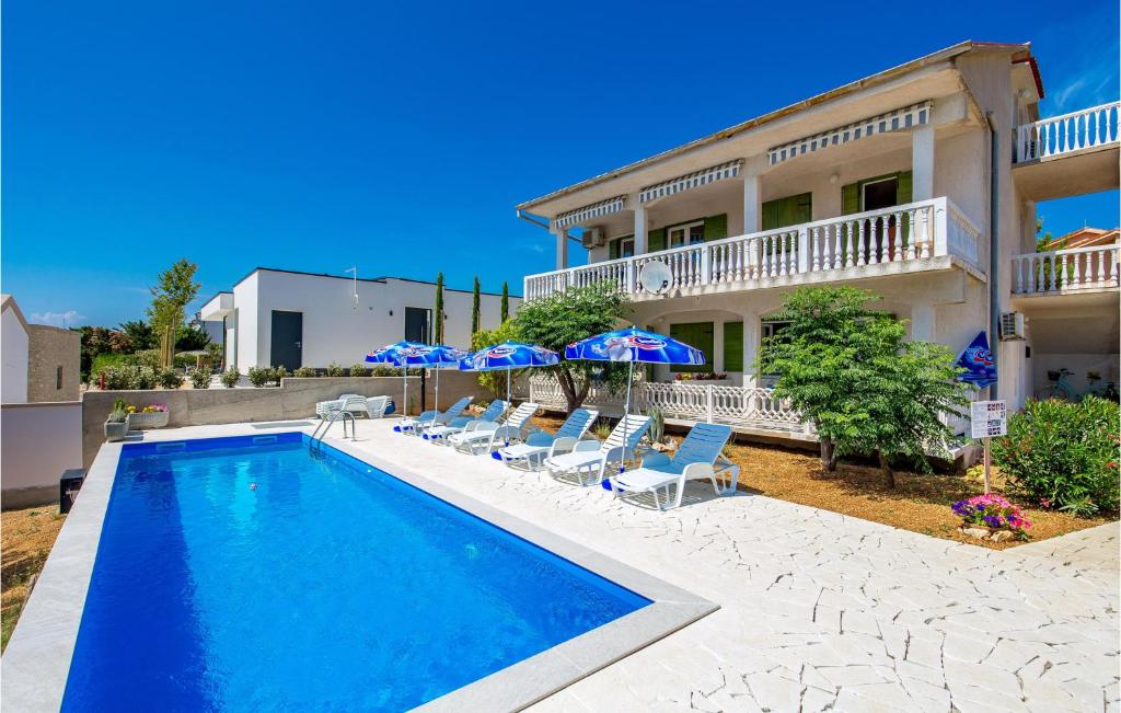a swimming pool with chairs and umbrellas in front of a house at Beautiful Apartment In Barbat Na Rabu With Outdoor Swimming Pool in Barbat na Rabu