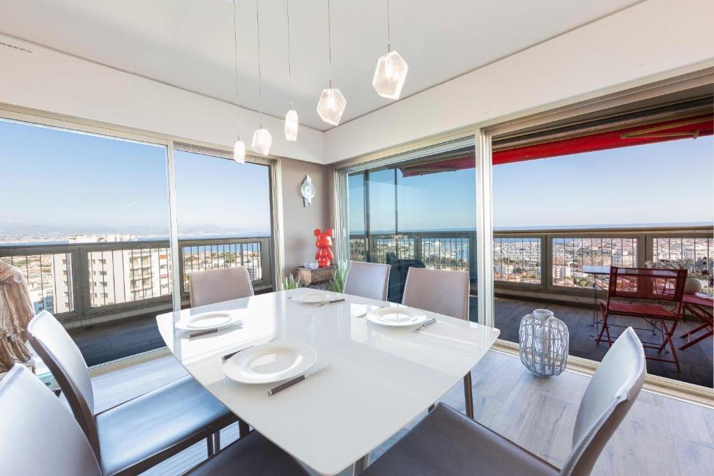 uma sala de jantar com uma mesa e cadeiras brancas e janelas grandes em BNB RENTING breathtaking view 2 bedroom apartment in Antibes ! em Antibes