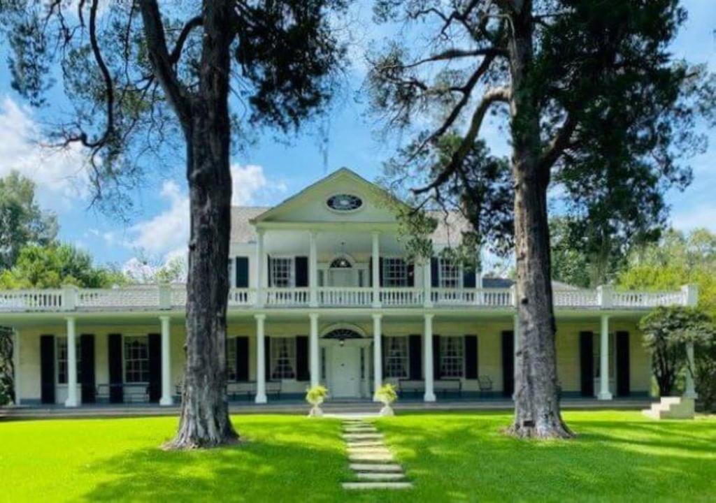 Linden - A Historic Bed and Breakfast في ناتشيز: بيت أبيض كبير وبه أشجار في الفناء