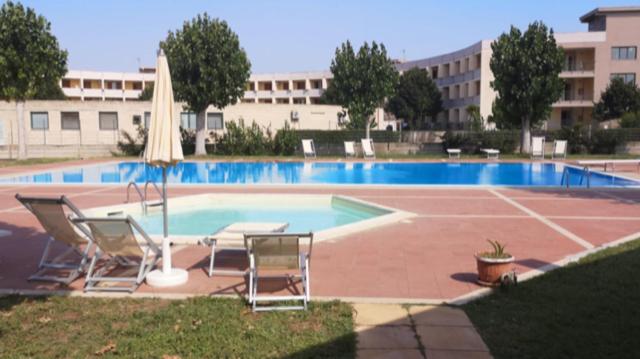 a swimming pool with two chairs and an umbrella at Villetta a schiera in villaggio Metatur in Metaponto