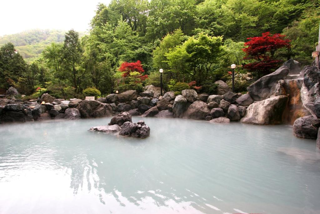 uma piscina de água com pedras e árvores em Hotel Mahoroba em Noboribetsu