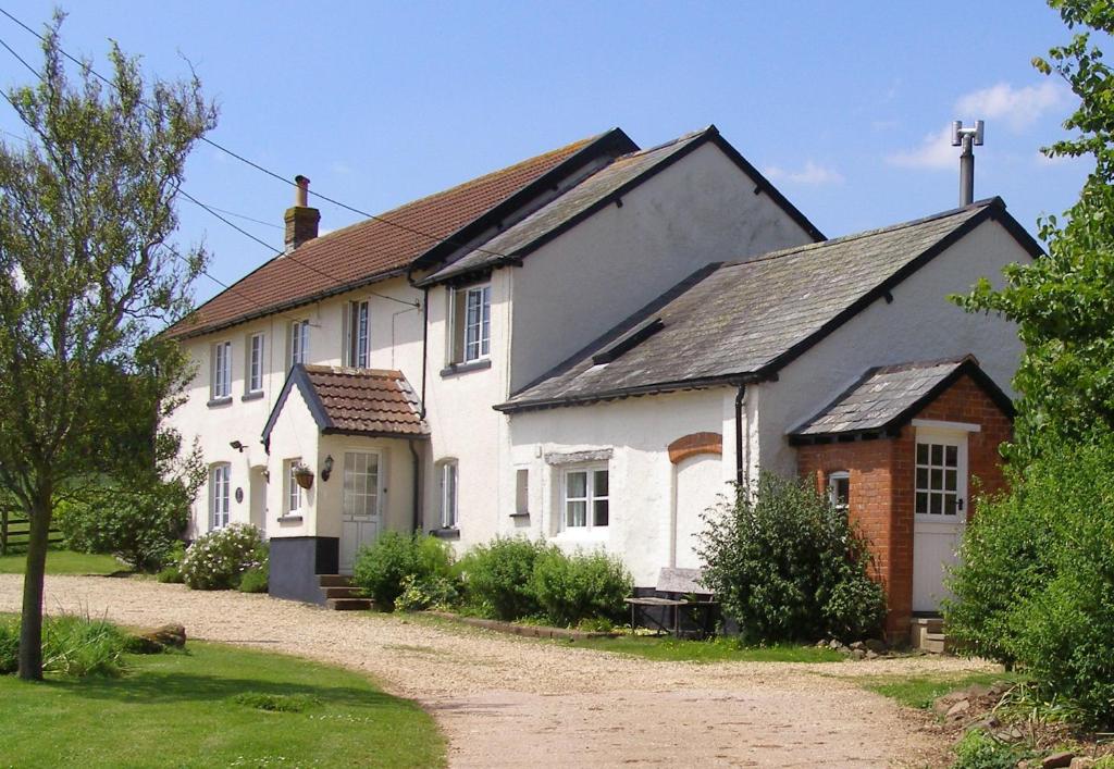 uma casa branca com um telhado preto em Highdown Farm Holiday Cottages em Cullompton