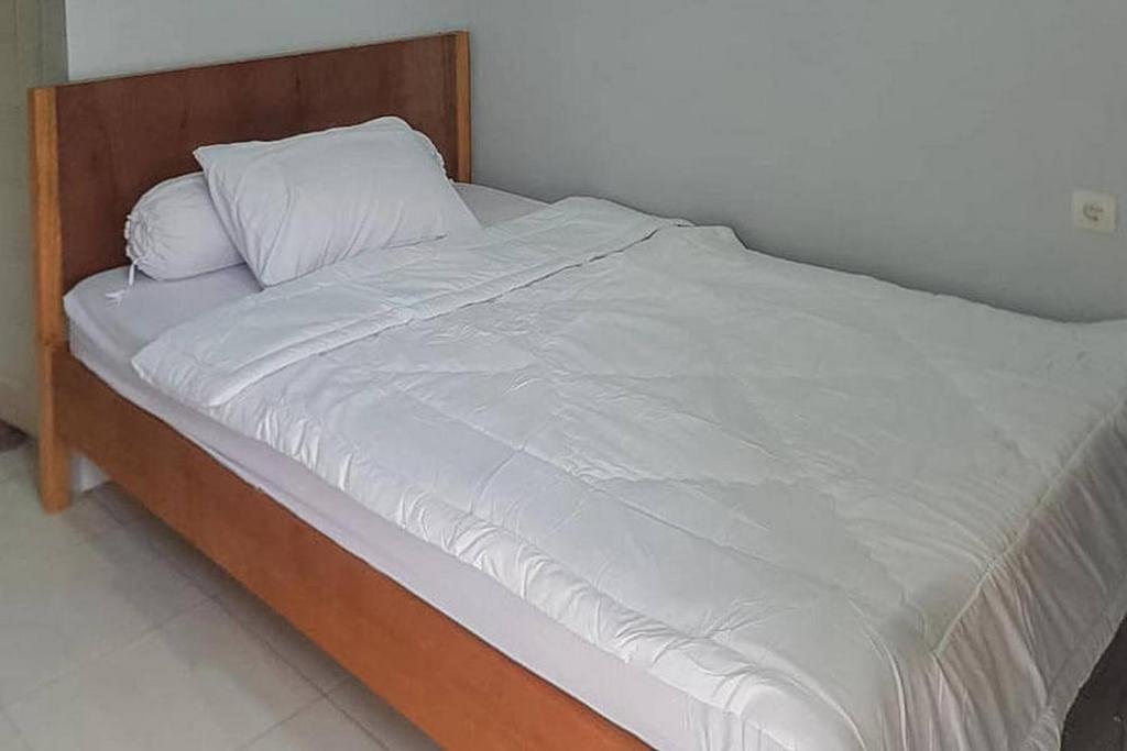 Elle comprend un grand lit avec des draps et des oreillers blancs. dans l'établissement Kai Homestay Near Anyer Beach RedPartner, à Kareo