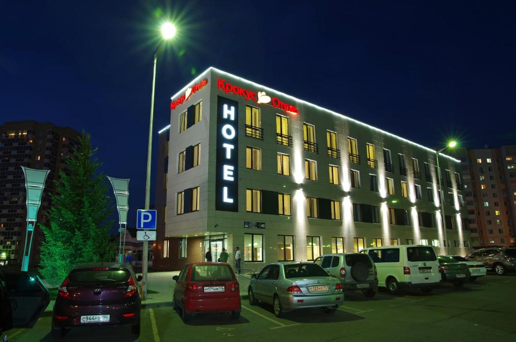 een groot gebouw met auto's geparkeerd op een parkeerplaats bij Hotel Krokus in Naberezhnyye Chelny
