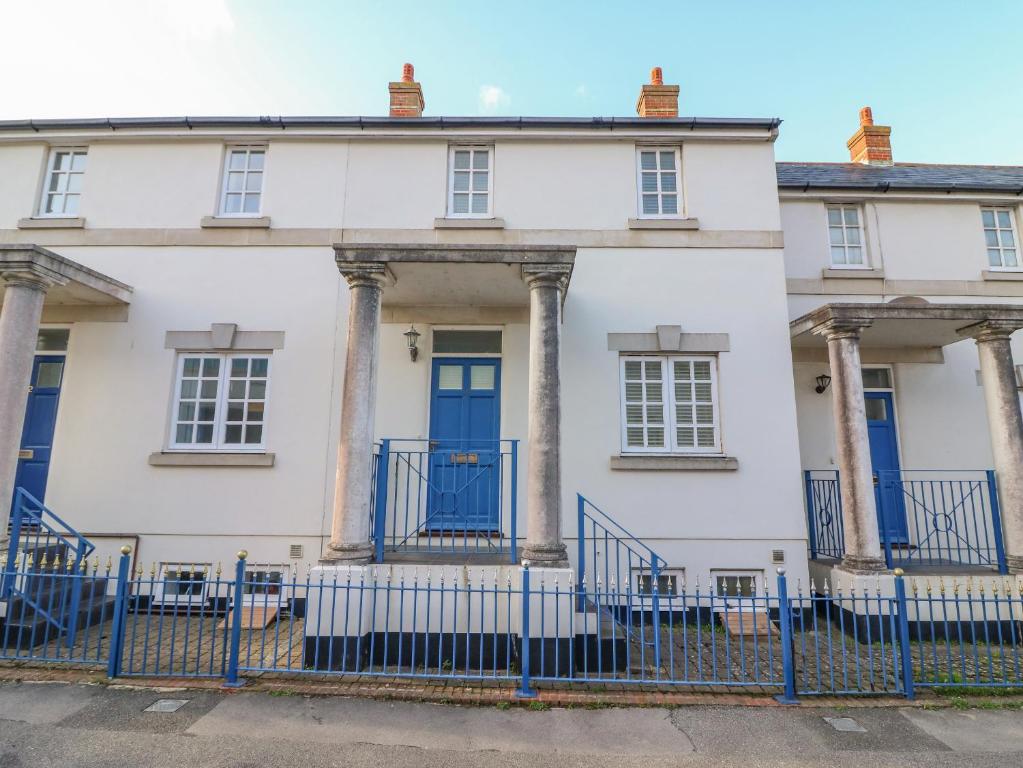 een wit huis met blauwe deuren en zuilen bij Hops House in Weymouth
