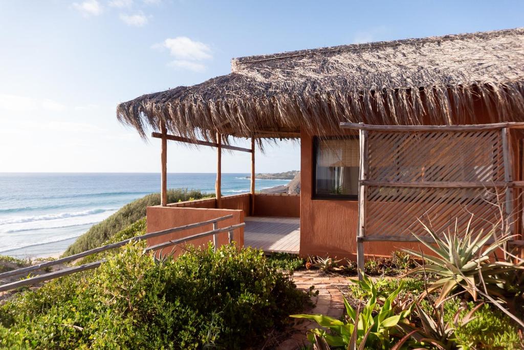 una casa sulla spiaggia con tetto di paglia e l'oceano di Bela Flor Beach Front Apartments a Inhambane