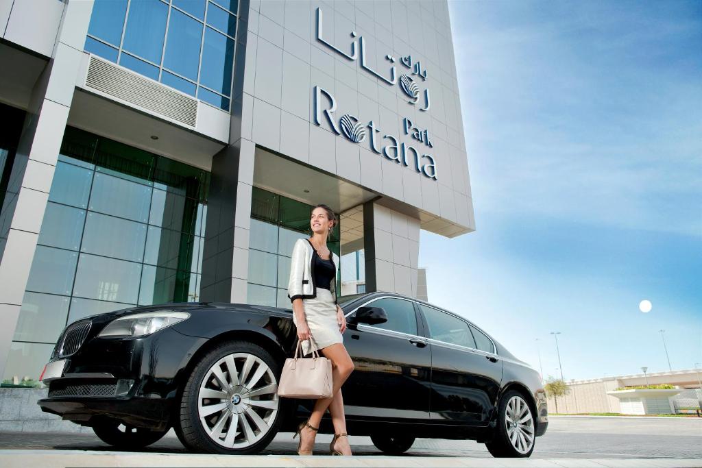 a woman standing next to a black car in front of a building at Park Rotana Abu Dhabi in Abu Dhabi