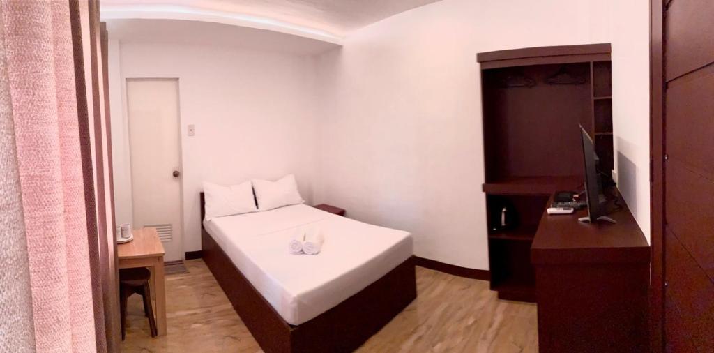 a small bedroom with a white bed and a piano at Kampotel Davao in Davao City
