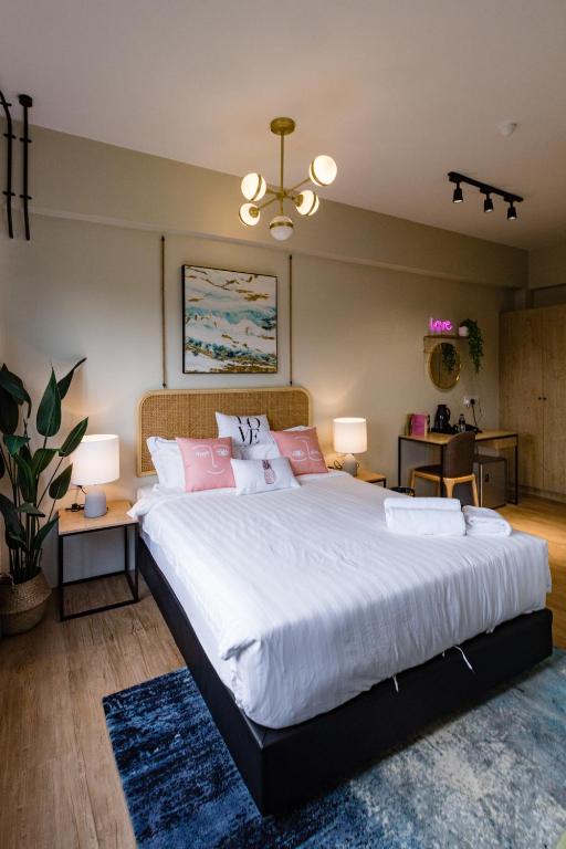 A bedroom with a large white bed, bedside lamps, desk, and patterned rug.
