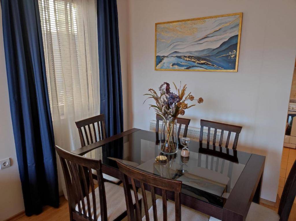 a dining room table with chairs and a vase of flowers at Neviasta Apartment in Smolyan