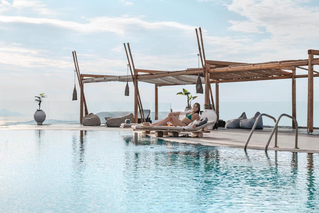 una mujer sentada en el borde de una piscina en un resort en Orizontes Hotel Santorini en Pirgos