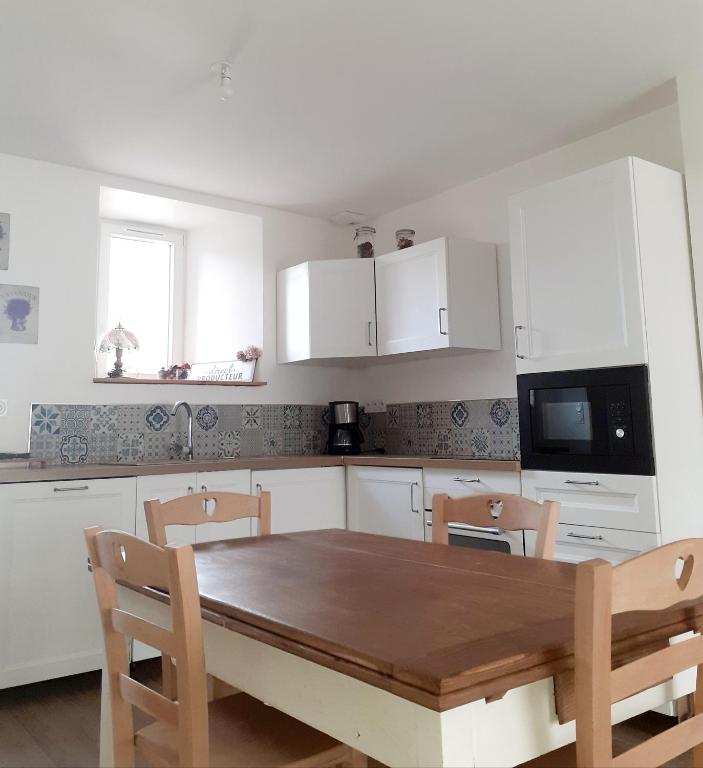 une cuisine avec une table en bois et des armoires blanches dans l'établissement Au Lutin Pommé - Maison de vacances Bretagne, à Mellé