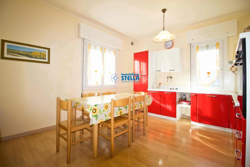 cocina con mesa, sillas y armarios rojos en Condominio Eden en Lido di Jesolo