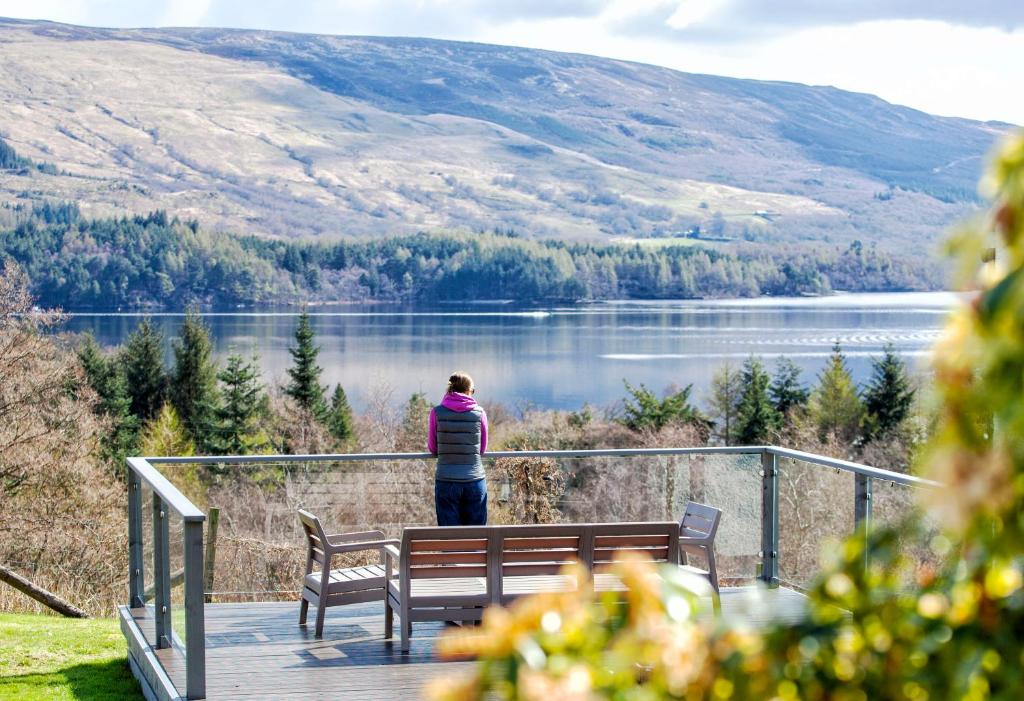 uma pessoa de pé num deque com vista para um lago em The Corries B&B em Luss