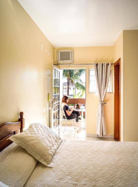 a woman sitting at a table in a bedroom at Costabela Apart Hotel e Pousada in Ilhabela