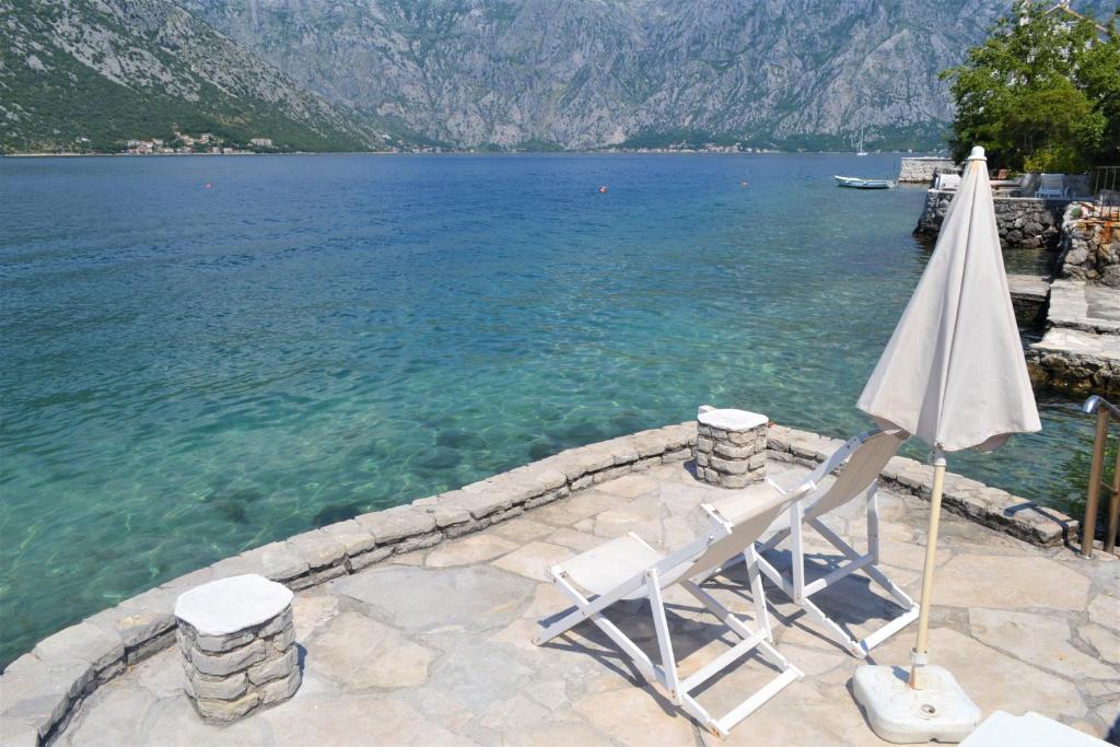 two chairs and an umbrella on the edge of a body of water at Apartments Djurovic in Kotor