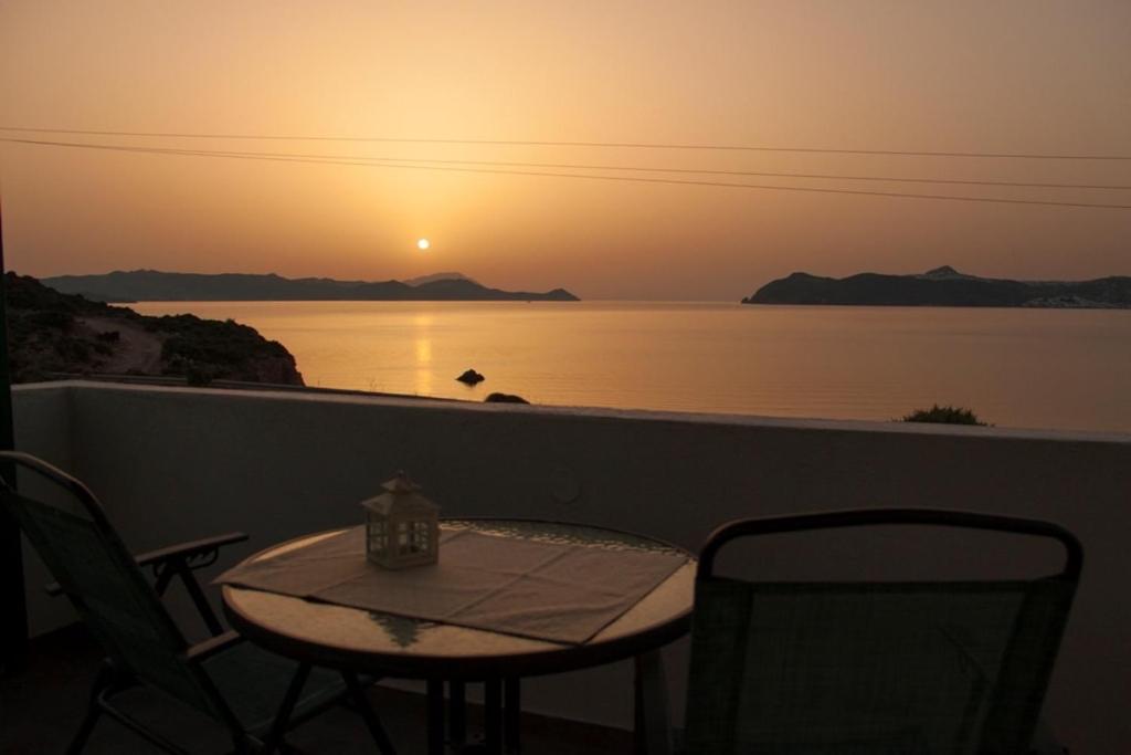 een tafel en stoelen op een balkon met uitzicht op de zonsondergang bij Akrothalassia in Adamas