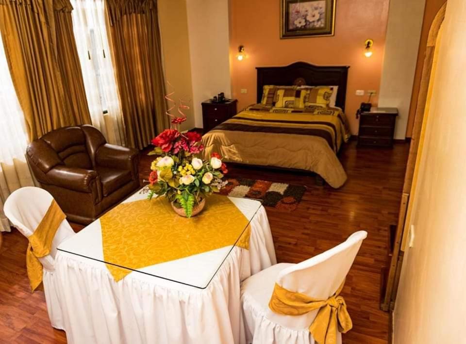 Un dormitorio con una cama y una mesa con flores. en Hotel Los Ilinizas en Latacunga