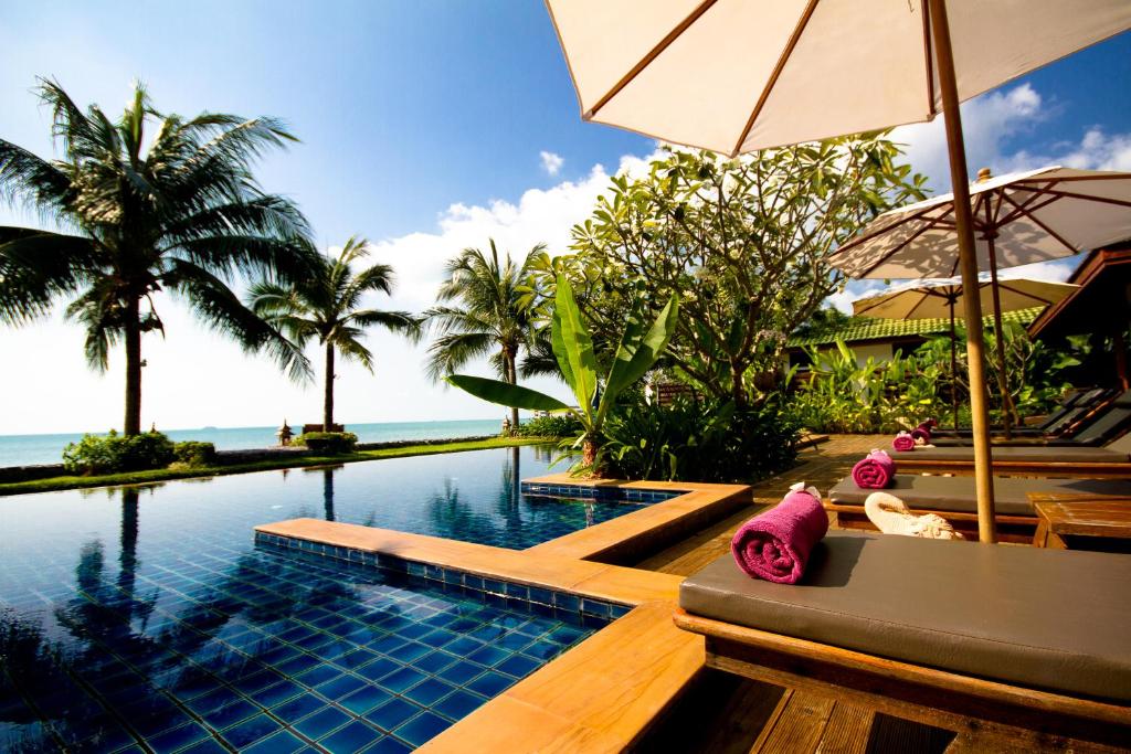 a swimming pool with an umbrella and some palm trees at Baan Phulay Luxury Beachfront Villa in Lipa Noi