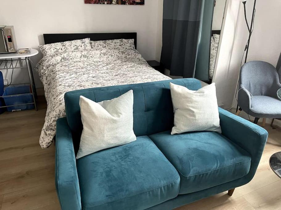 ein blaues Sofa mit weißen Kissen im Schlafzimmer in der Unterkunft Studio Flat London Finchley Rd NW11 in London