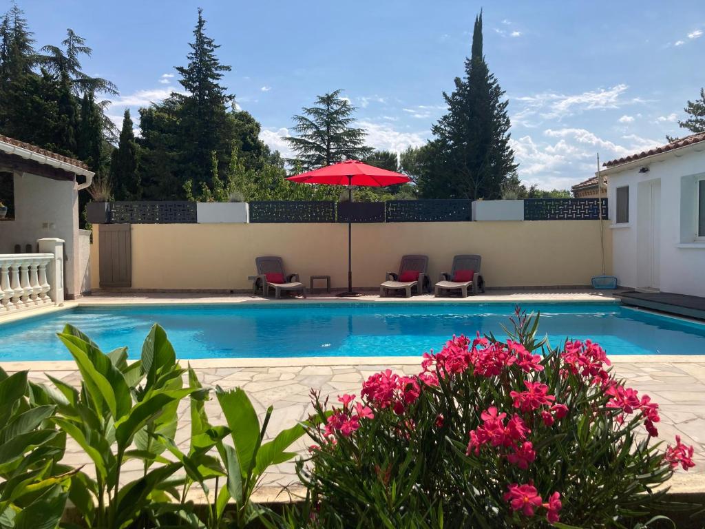 a swimming pool with a red umbrella and pink flowers at Au pont des Charettes - Villa piscine et SPA in Uzès
