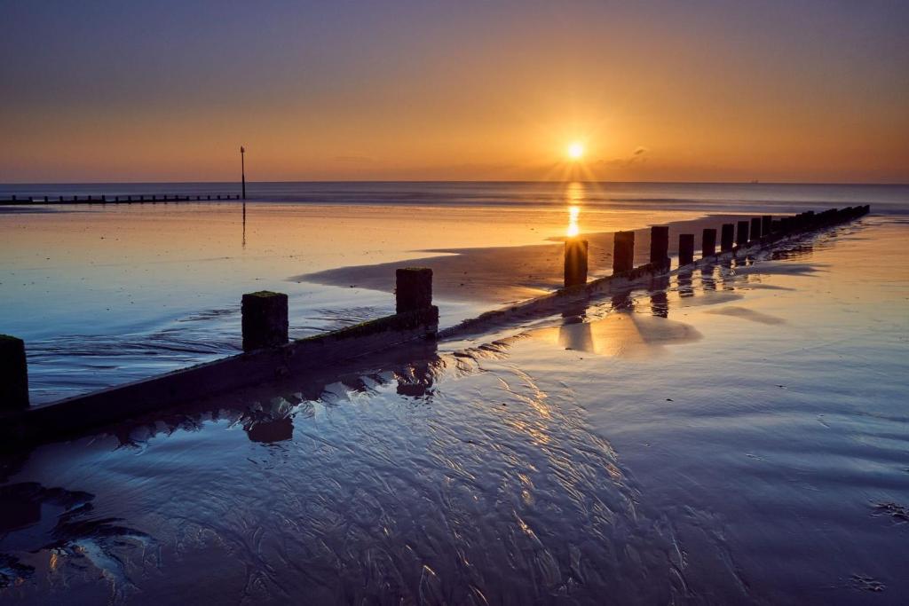 a pier on the water with the sunset in the background at The Annex Dymchurch in Dymchurch