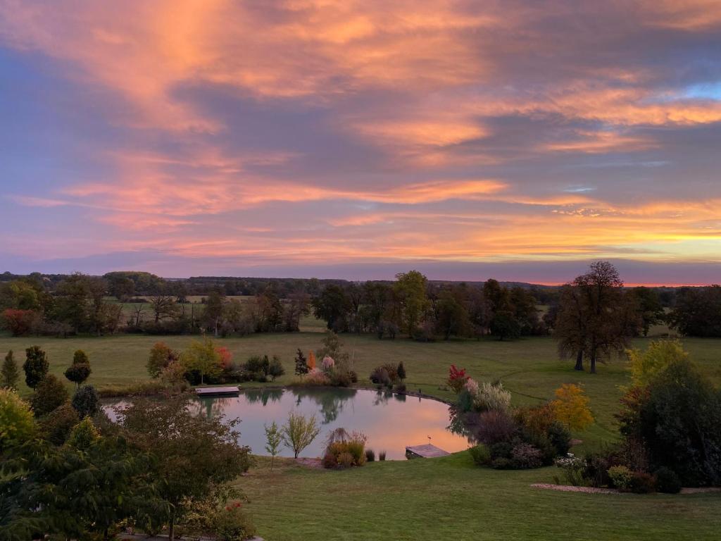 a view of a pond in a field with a sunset at B&amp;B Château de Preuil in Vallenay