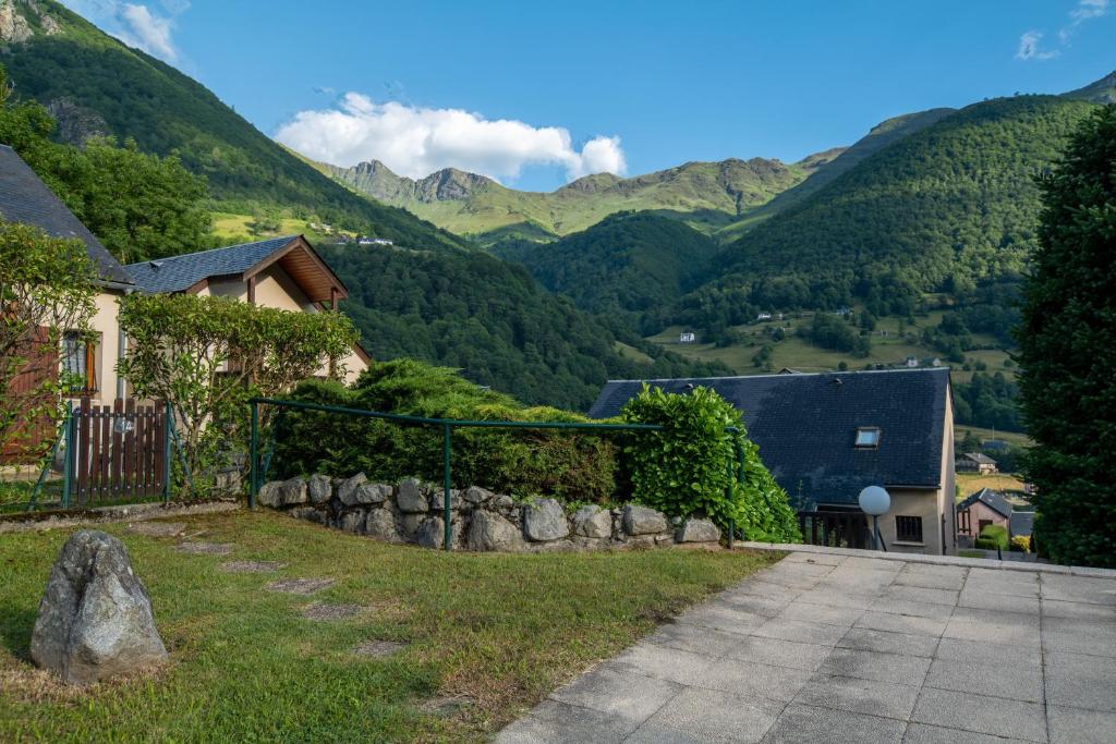 a house with a stone fence and mountains in the background at Chalet mitoyen tout confort in Cauterets