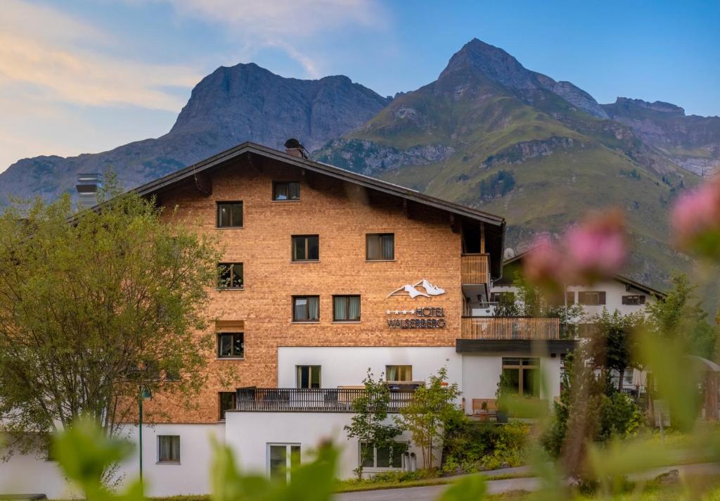 a large brick building with mountains in the background at Hotel Walserberg in Warth am Arlberg