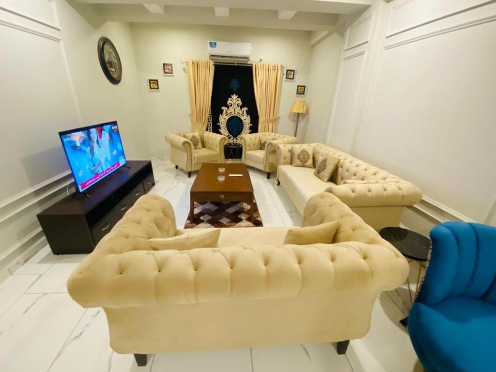 Holidazzle Serviced Apartments Bahria Town في روالبندي: غرفة معيشة مع كنب وتلفزيون بشاشة مسطحة