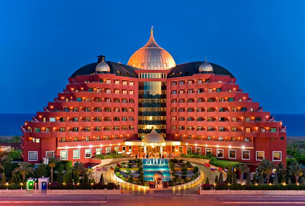 een groot rood gebouw met een zwembad ervoor bij Delphin Palace Hotel in Lara