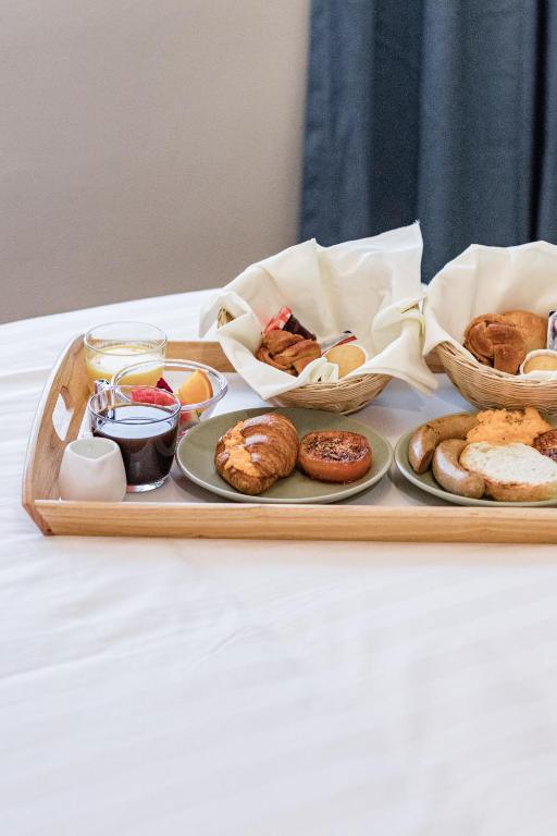 A breakfast tray arranged with pastries, fruit, jam, and bread on a bed.