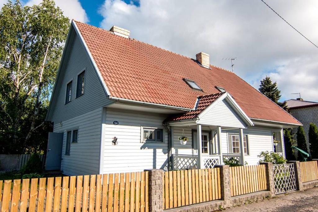 a white house with a red roof behind a fence at Manni Homestay in Kuressaare