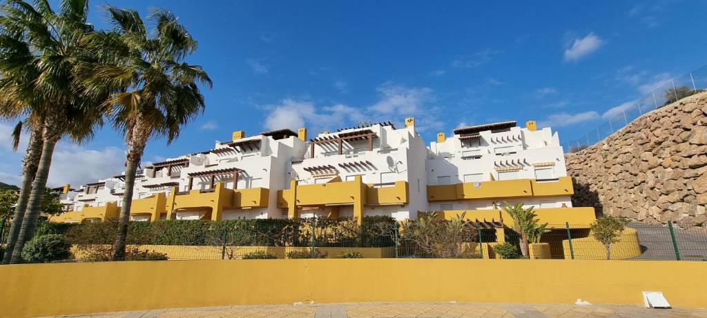 ein weiß-gelbes Gebäude mit Palmen davor in der Unterkunft Homes of Spain, Atico Lomas del Mar V con vistas al mar y solárium grande, WIFI in Playas de Vera