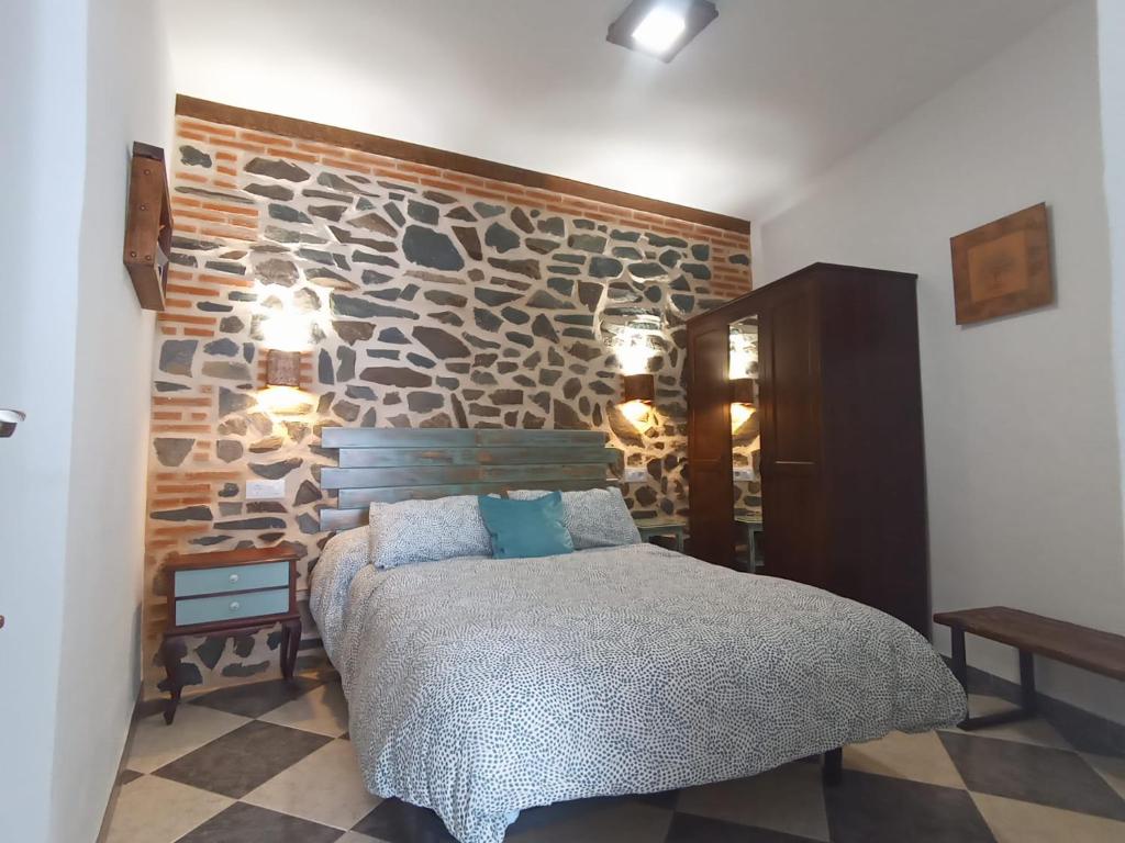 1 dormitorio con 1 cama y pared de piedra en Casa Monte Los Peñasquitos, en Cazalla de la Sierra