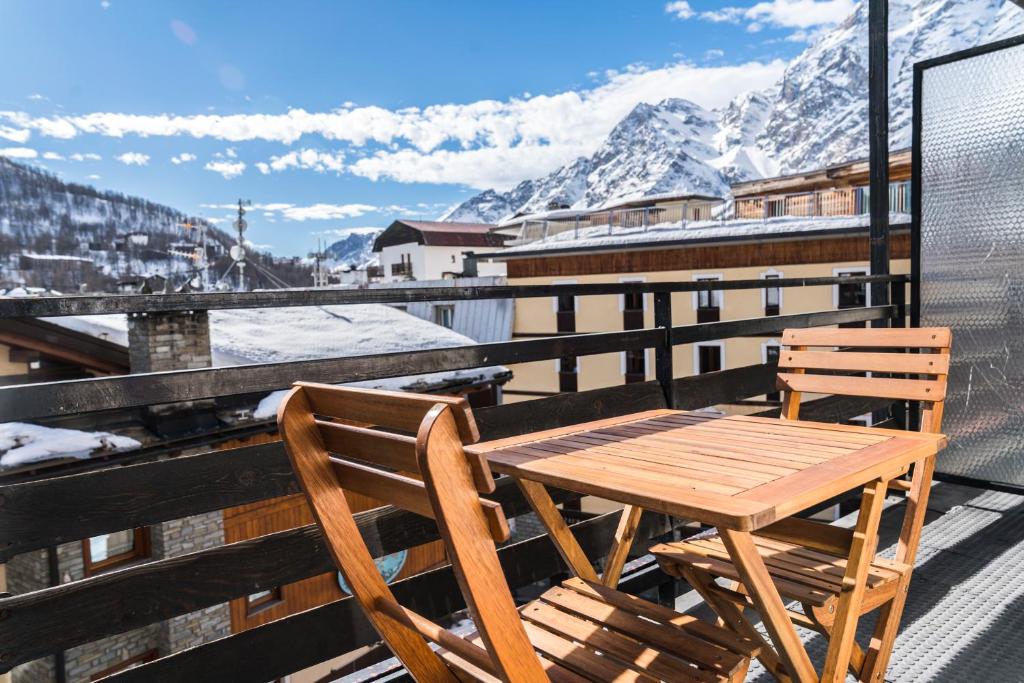 a wooden table and chairs on a balcony with snow covered mountains at Stay in Cervinia Deluxe Apartment in Breuil-Cervinia