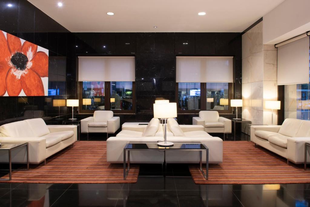 A formal lounge offers white armchairs and sofas around low tables beneath large windows.