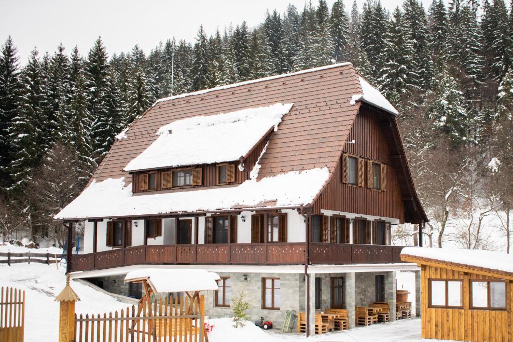 ein schneebedecktes Haus mit Bäumen im Hintergrund in der Unterkunft Pensiunea Agroturistică Erdélykincse Panzió in Sicasău