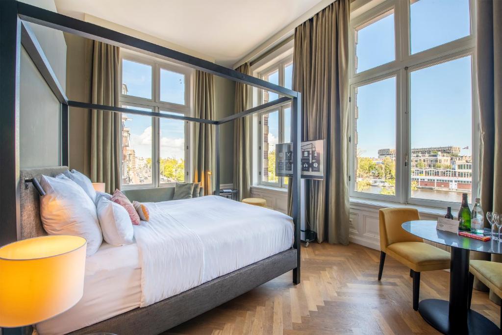 a hotel room with a bed and a desk and windows at Pestana Amsterdam Riverside in Amsterdam