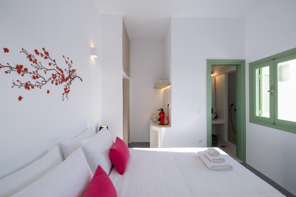 a white bedroom with a white bed with red pillows at White Orchid Cave House & Studio in Pirgos