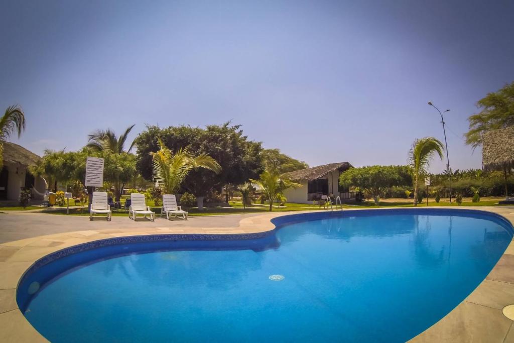 a large blue swimming pool with chairs and palm trees at La Choza Bungalows in Tambo Grande